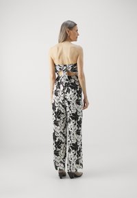 Gėlių jumpsuit'as su juodai baltu be petnešėlių dizainu, turintis užsegimą nugaroje, plačias kelnes ir laisvą siluetą.