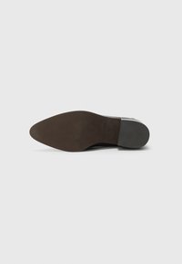 Semelle de chaussure en cuir noir avec un orteil pointu, dotée de rainures de traction en caoutchouc et d'une base texturée marron pour la stabilité.