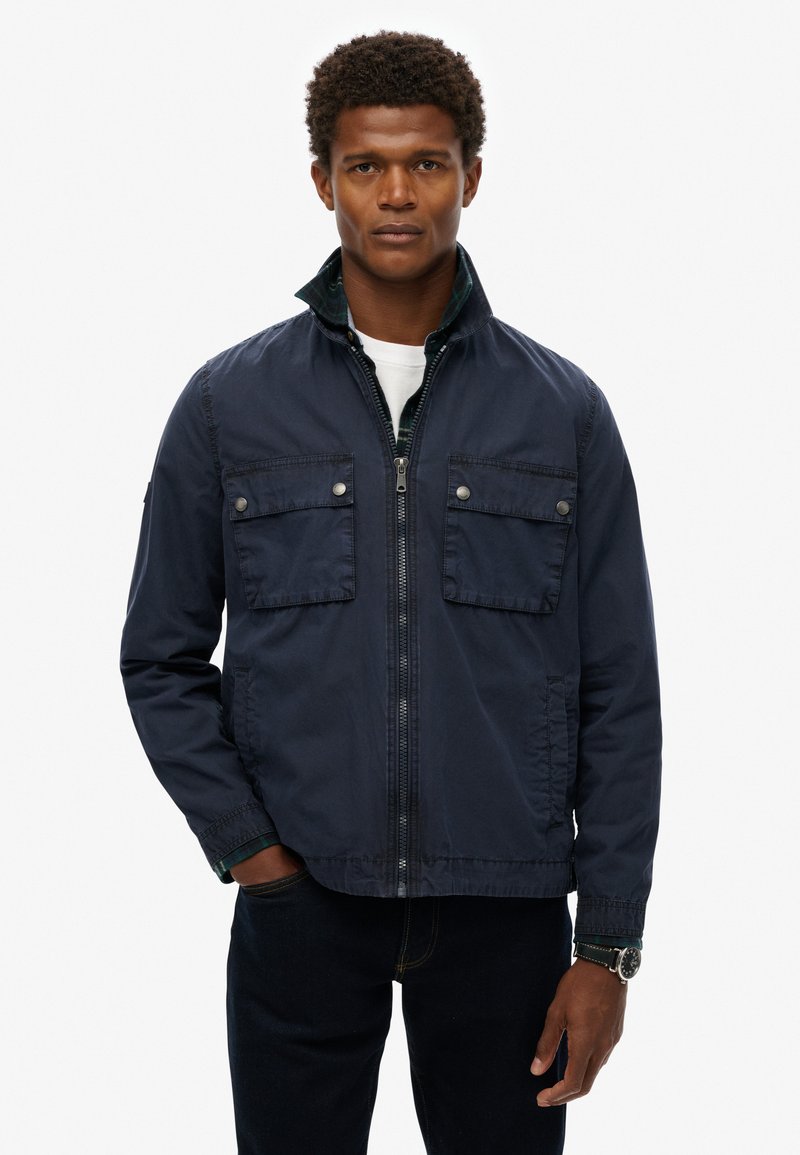Navy blue zip-up jacket with two front flap pockets, a high collar, and contrasting green inner lining. Made of lightweight fabric.