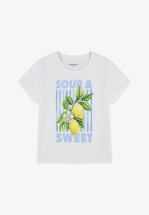 Tricou alb din bumbac cu grafică colorată de lămâie, frunze verzi și textul „ACRU ȘI DULCE” pe fundal cu dungi verticale albastre.