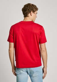 Red cotton T-shirt with a crew neck and short sleeves, featuring a straight hem and a plain design. Worn with light blue jeans.