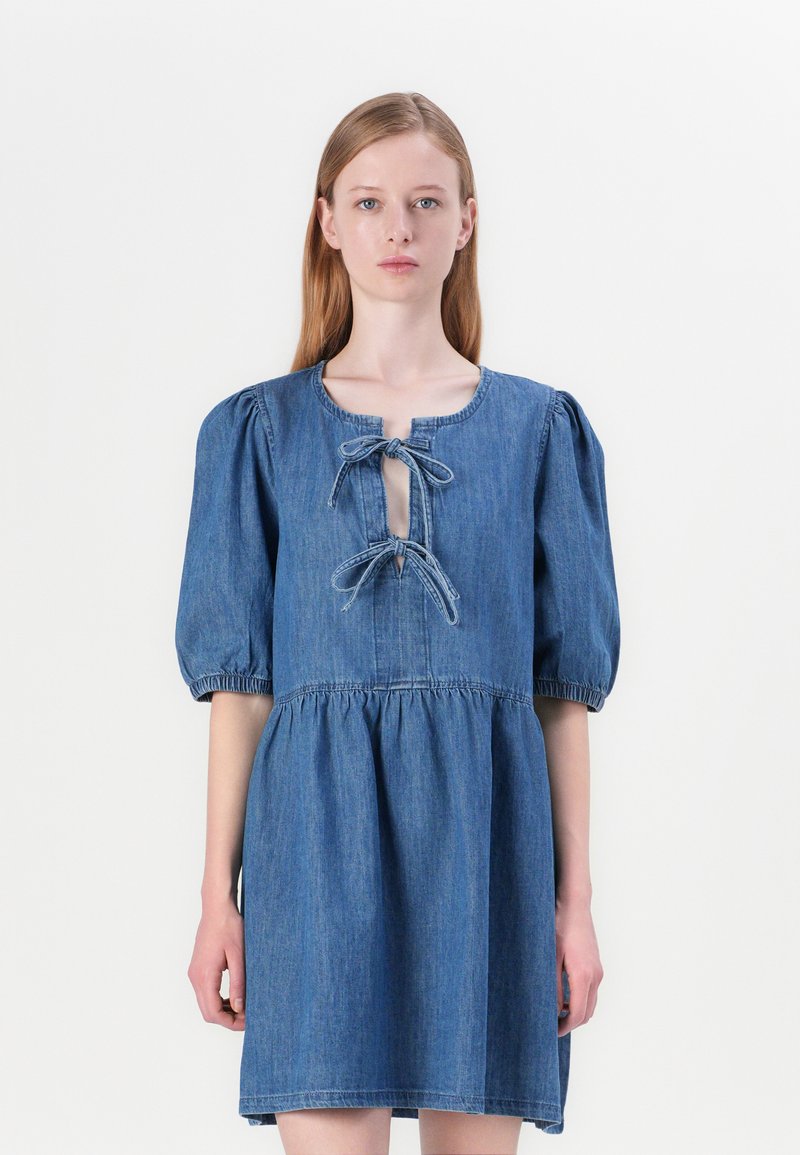 Denimkjole med innsnevret midje, puffermer og knytetekst i halsen. Har en knelength hem og et mykt, teksturert stoff.
