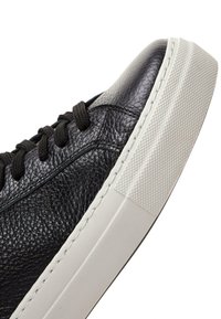 Zwarte leren sneaker met een gestructureerd oppervlak, ronde veters en een dikke witte rubberen zool met een grippatroon.