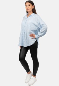 Lichtblauwe button-up shirt met witte stippen, oversized pasvorm, gecombineerd met zwarte leggings en witte sneakers. Zachte, gestructureerde stof.