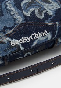 Borsa in tessuto con motivo floreale blu e cuciture crema, con logo "SeeByChloé" e una tracolla in pelle liscia di colore blu navy.