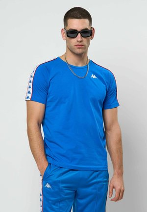 Μπλε αθλητική μπλούζα Kappa με κοντά μανίκια, με κόκκινες πλευρικές ρίγες σε αντίθεση και λευκό λογότυπο Kappa στο στήθος και τα μανίκια.