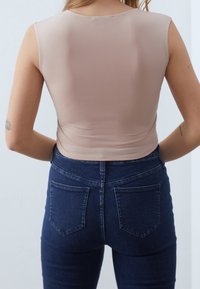 Naken, figursydd ärmlös topp av mjukt material, tillsammans med mörkblå denimjeans med bakfickor och hög midja.