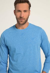 Blauw langemouwen t-shirt met een gestructureerde, gemêleerde afwerking. Voorzien van een ronde halslijn en aansluitende mouwen. Subtiel logo-detail op de borst.