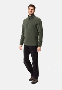 Pulover din fleece verde închis cu guler cu fermoar pe jumătate, țesătură texturată, asortat cu pantaloni negri și bocanci de drumeție rezistenți.