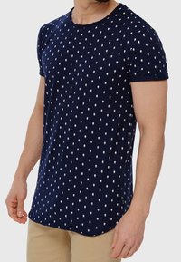 Camiseta de algodón azul marino de manga corta, con un patrón blanco de diamantes y un dobladillo redondeado. Textura suave, ajuste informal.