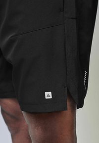 Black athletic shorts featuring a smooth fabric, side mesh panels for breathability, and a small white logo at the hem.