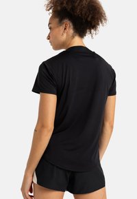 Camiseta deportiva negra de manga corta, hecha de una tela suave, con un cuello redondo y un corte holgado, combinada con pantalones cortos negros.