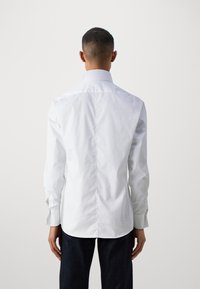 Witte lange mouwen blouse met een klassieke kraag, gladde textuur en knoopmanchetten. Heeft een rechte achternaad en een getailleerde pasvorm.