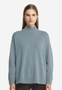 Ljusblå, överdimensionerad tröja med hög ribbad krage, sänkta axlar, ribbade ärmslut och nederkant, tillverkad av ett mjukt, texturerat stickat tyg.