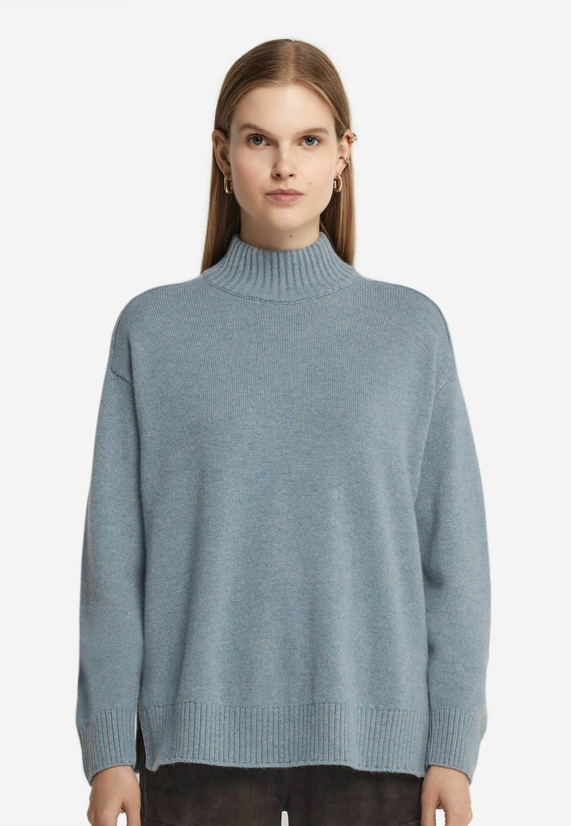 Ljusblå, överdimensionerad tröja med hög ribbad krage, sänkta axlar, ribbade ärmslut och nederkant, tillverkad av ett mjukt, texturerat stickat tyg.