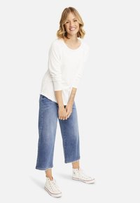 Weißes Langarmshirt, lockere Passform, kombiniert mit hellblauen weit geschnittenen Jeans und weißen High-Top-Sneakers. Glatte Textur, lässiges Design.