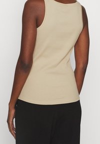 Beige ribbad linne med rund halsringning och breda axelband, figurnära design, visad bakifrån mot en neutral bakgrund.