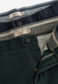 Drei Paar schmale Hosen aus Stoff in den Farben Grün, Marineblau und Grau. Mit Knöpfen, Reißverschlüssen und kontrastierenden gestreiften Futter.