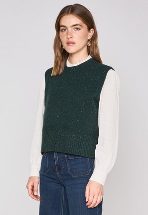 Maglione senza maniche lavorato a maglia di colore verde scuro con orlo a coste, decorato con macchie multicolori. Indossato sopra una blusa bianca a maniche lunghe con volant.