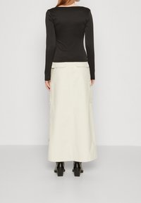 Černý žebrovaný top s dlouhým rukávem spárovaný s krémovou maxi sukní s bočními kapsami, texturovanou tkaninou a černými vysokými botami na kotníku.