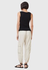 Zwarte mouwloze top gecombineerd met lichtbeige cargobroek met zijzakken en elastische cuffs; sandalen met een geschoende ontwerpen.
