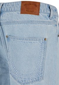 Blugi din denim de culoare albastru deschis, cu o etichetă din piele la talie, buzunare spate cu cusături duble albe și accente de nituri metalice.