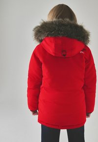 Röd parkabyxa med foder av päls, med låsning, elastiska muddarna och en slät, matt yta. Inga synliga logotypdetaljer.