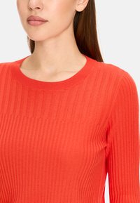 Roter gerippter Strickpullover mit rundem Ausschnitt und langen Ärmeln. Verfügt über vertikale Streifen und eine weiche Textur.