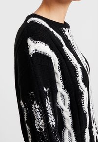 Black knitted sweater with white cable knit patterns, featuring a round neckline and long sleeves, showcasing textured details.