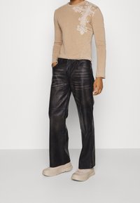 Beige långärmad topp med blommönster och svarta läderbyxor med vida ben. Byxorna har en blank yta och sömdetaljer.