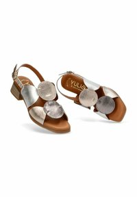Sandalias de tacón marrones con diseño de tipo slingback, que cuentan con tres acentos metálicos redondos en plata y bronce en las correas frontales.