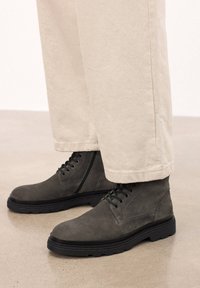 Botines de ante gris con suelas de goma negras y diseño con cordones, combinados con pantalones de pierna ancha en color beige claro.