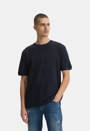 T-shirt blu navy a maniche corte con scollatura rotonda e texture a costine. Abbinato a jeans chiari strappati.