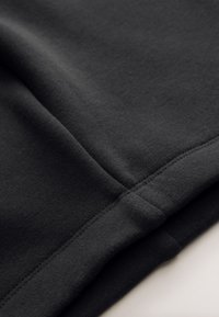 Tessuto in felpa di cotone nero, che mostra una texture liscia con cuciture ricamate e un dettaglio di orlo piegato.