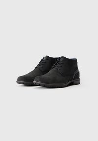 Botas de cuero negras hasta el tobillo con cordones y suela resistente, posicionadas una al lado de la otra sobre un fondo blanco liso.