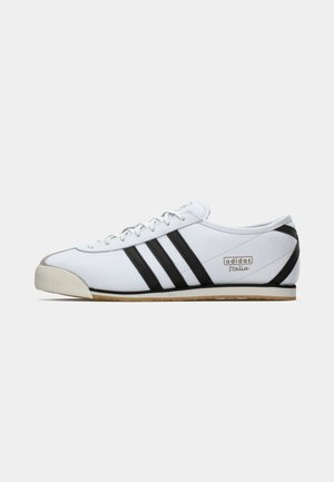 Bijela tenisica s tri crne pruge, gumeni prednji dio i teksturirana potplat. Brand logo "adidas Italia" s strane, minimalistički dizajn.