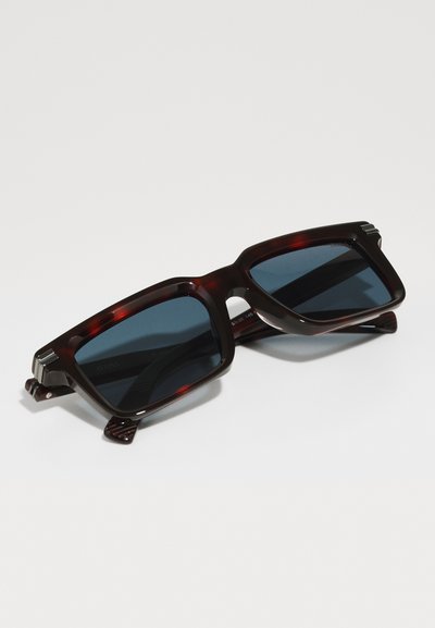 Tortoiseshell sunglasses with rectangular frames, dark lenses, and textured accents on the temples. The design features a bold, angular shape.