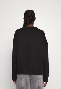 Black oversized sweatshirt with a round neckline and dropped shoulders, featuring a textured finish, paired with light gray distressed jeans.