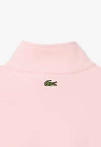 Polo shirt rosa a pois con una texture morbida, caratterizzato da un logo di coccodrillo ricamato in verde sul colletto posteriore. Design classico con colletto a pieghe.