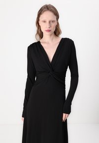 Black long-sleeve dress with a deep V-neck and twisted waist design. Soft, stretchy fabric with a flowing silhouette. Smooth texture.