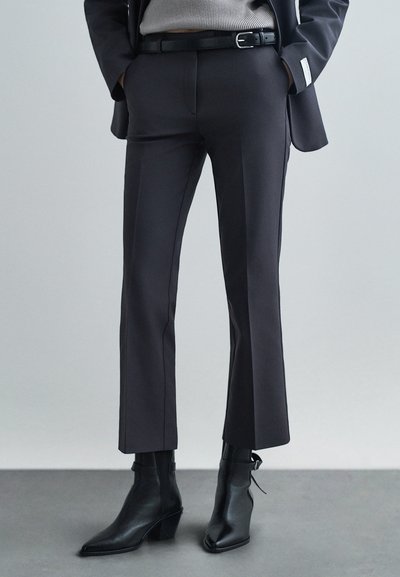 Pantalon noir ajusté avec une coupe droite, présentant une texture lisse et des détails minimalistes, associé à des bottines noires à talons pointus.