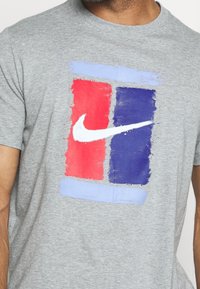 Graues Baumwoll-T-Shirt mit einem gemalten Design in roten, blauen und hellblauen Blöcken sowie einem weißen Nike-Logo in der Mitte.