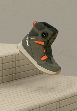 Stivale Viking Gore-Tex verde oliva e arancione con lacci a rotella BOA, mostrato sospeso sopra delle scale piastrellate beige.