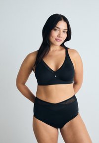 Ensemble de lingerie noire comprenant un soutien-gorge à décolleté en V avec des accents transparents, accompagné de culottes taille haute. Texture de tissu douce.