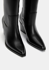Svarta läderankelboots med spetsiga tår och låg blockklack. Har subtila sömmar och en böjd design på sidorna.