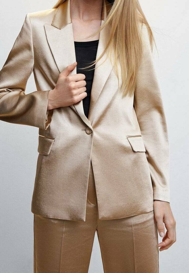 Béžový saténový blazer s jedním knoflíkem, klopami a dvěma předními kapsami. Hladká textura a přiléhavý střih, spárovaný s černým topem.