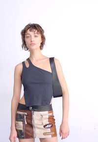 Top corto nero a coste con design asimmetrico, dotato di un'apertura sulla spalla e di una tracolla in pelle. Abbinato a una gonna marrone a più pannelli.