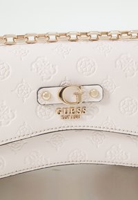 Borsa a tracolla in faux leather bianco goffrato con hardware dorato, caratterizzata da un logo prominente e una catena, texture liscia e motivi intricati.