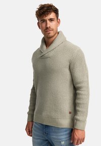 Suéter de punto gris claro con cuello de chal y patrón texturizado. Puños y dobladillo acanalados, con una pequeña etiqueta de marca en el lateral inferior.