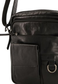 Schwarze Leder-Umhängetasche mit einem Reißverschluss-Hauptfach, einer Fronttasche, strukturierten Oberflächen und einem runden Metalldetail. Mit bedrucktem Logo.